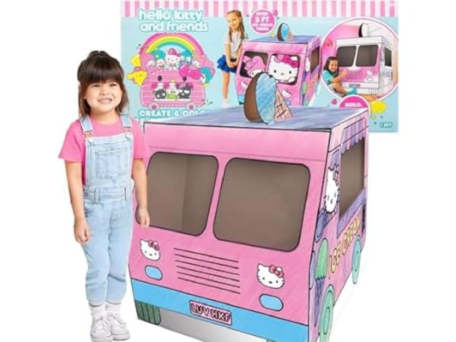 A child standing next to a Hello Kitty themed pink cardboard play ice cream truck and its packaging.
