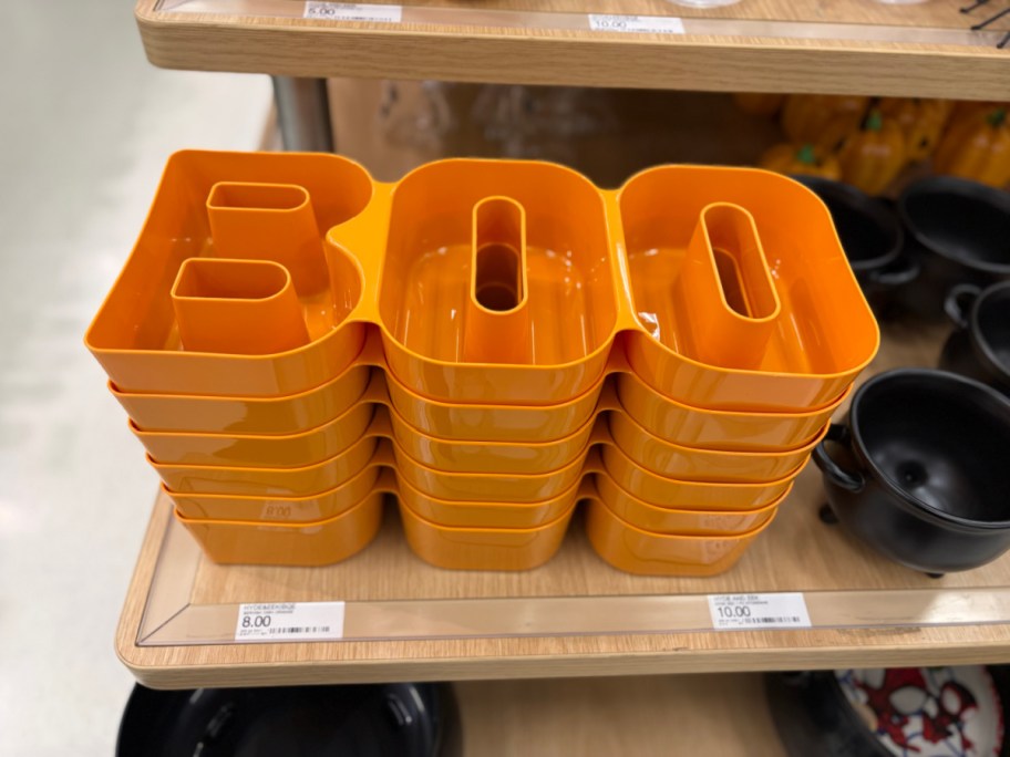 A stack of orange Hyde & EEK! Halloween figural BOO serving dishes on a store shelf.
