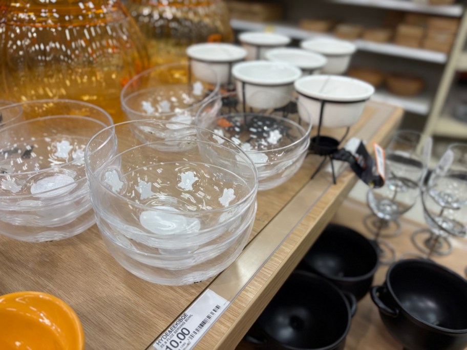 Stacks of clear glass Hyde & EEK! Halloween serving bowls decorated with white ghost icons displayed on a store shelf.