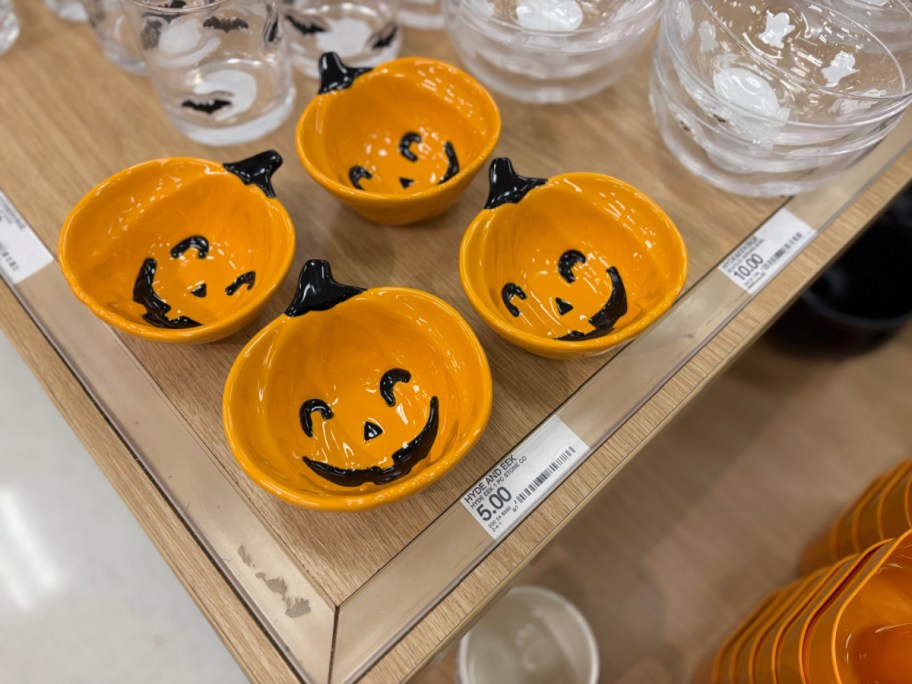 Four orange Hyde & EEK! mini pumpkin Halloween bowls with black jack-o'-lantern faces displayed on a store shelf.