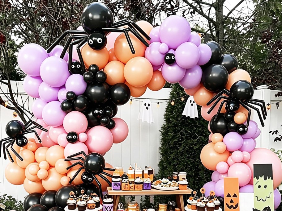 orange, pink, purple, and black balloon arch over a dessert table at a party