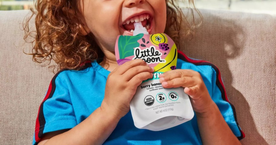 A young child in a blue shirt drinking from a Little Spoon smoothie pouch.