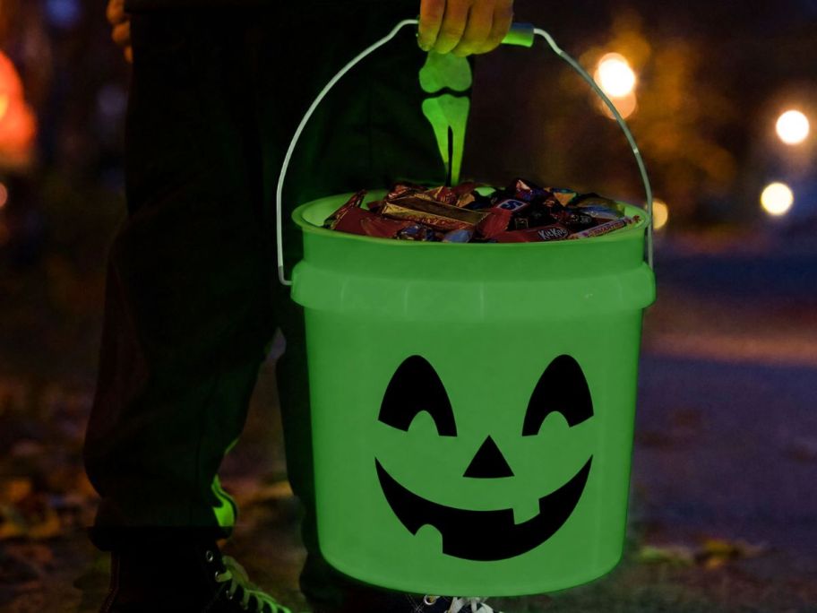 Child holding a glow in the dark lowe's halloween bucket filled with candy