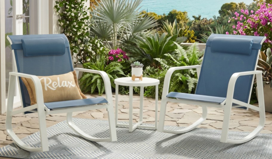 2 patio chairs and a small table on a patio with plants and water in background