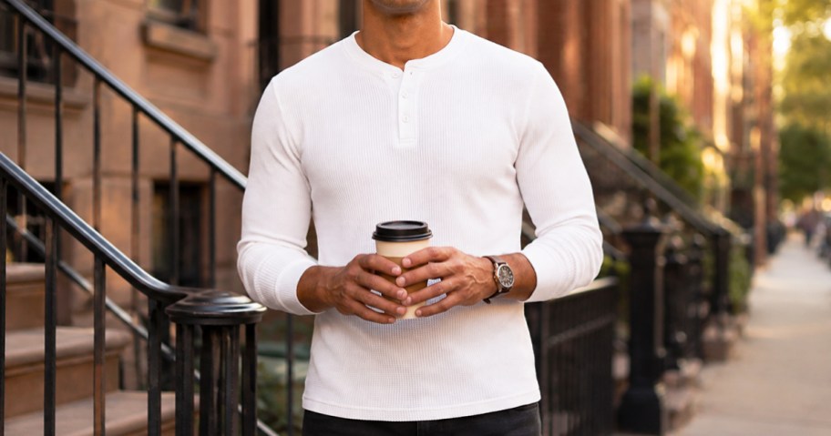 man wearing a white henley shirt holding a coffee