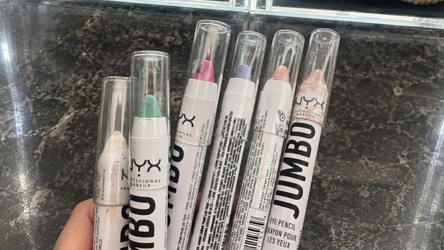 a hand holding an assortment of colored jumbo eye pencils