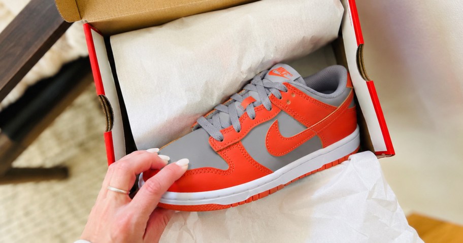 hand taking an orange and grey nike shoe out from a shoe box