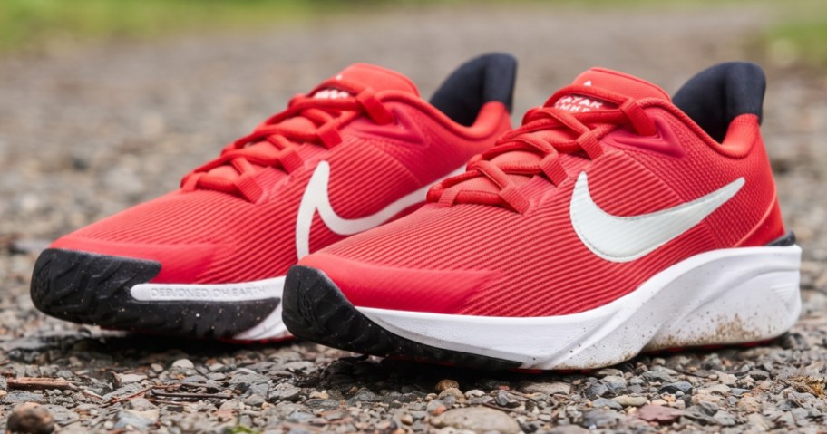 A pair of red Nike running shoes with white swooshes and white soles resting on a gravel path.
