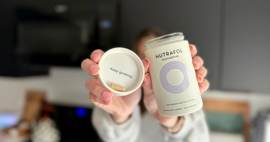 woman holding up a bottle and lid of Nutrafol postpartum hair supplements 