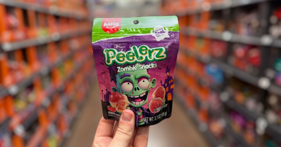 A hand holding a bag of Peelerz Zombie Snacks gummy candy in a store aisle.
