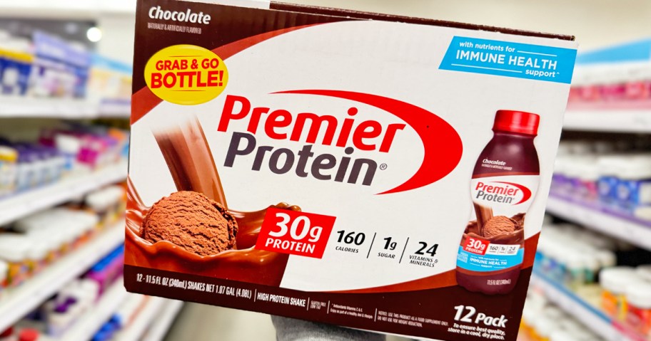 hand holding up a box of Premier Protein Shakes in store aisle