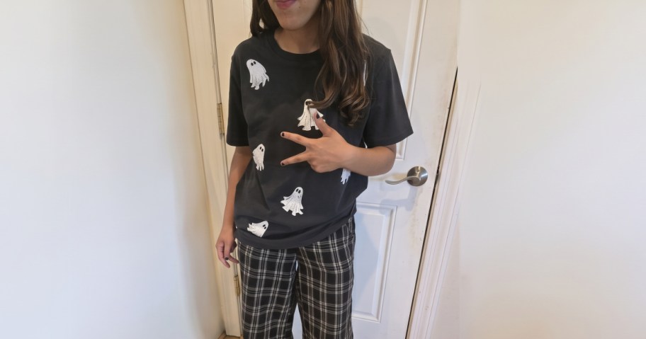 Woman wearing a black short-sleeve graphic tee with a white ghost pattern and plaid pants.
