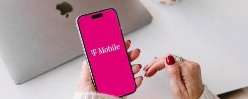woman holding a phone with T-Mobile on it with laptop in background