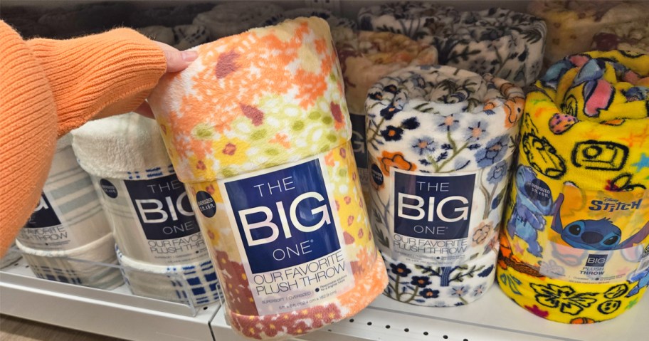 hand grabbing floral print throw blanket from store shelf