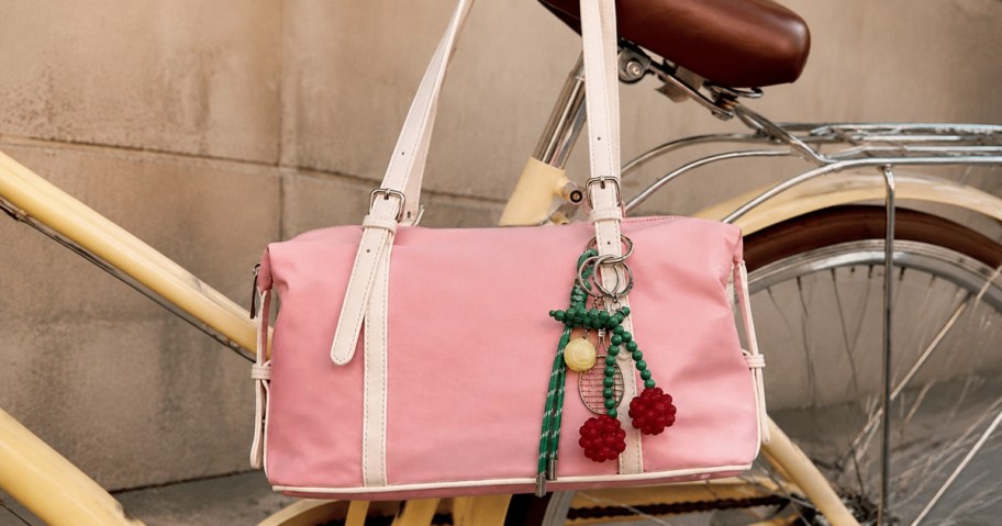 Pink shoulder bag with colorful cherry charm displayed on a yellow bicycle.