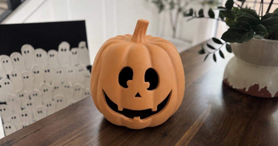 orange terracotta pumpkin sitting on dining room table with vase and ghost painting in background
