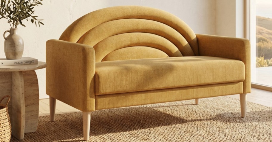 A yellow upholstered loveseat with a distinctive rainbow-arched channel-tufted backrest and light wooden legs, sitting on a jute rug.