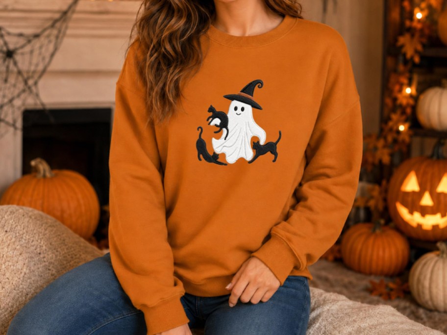 woman wearing an orange sweatshirt with ghosts and black cats embroidered on it