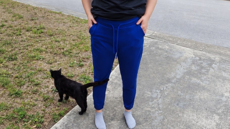 a woman wearing blue joggers next to a black cat