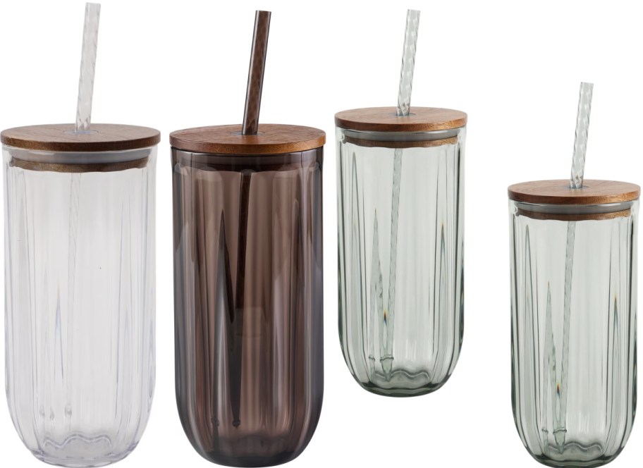 Four ribbed glass tumblers with wooden lids and straws displayed on a white background, featuring one clear, one amber, and two light green glasses.