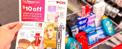 a CVS cart filled with beauty products and hand holding a sale flyer next to it