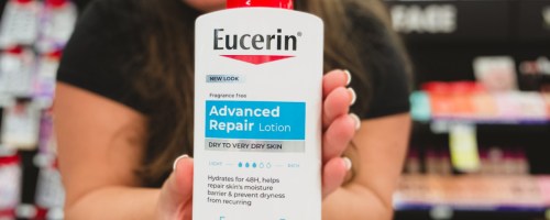 smiling woman holding up a bottle of eucerin body lotion in a store aisle