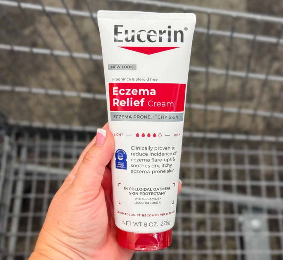 hand holding a bottle of eucerin cream above a shopping cart