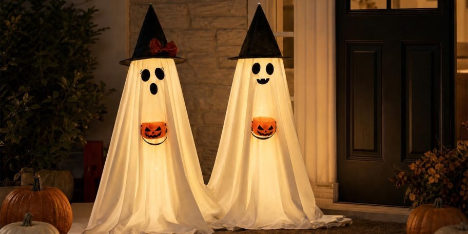 two ghosts holding pumpkins wearing black witch hats outside home 