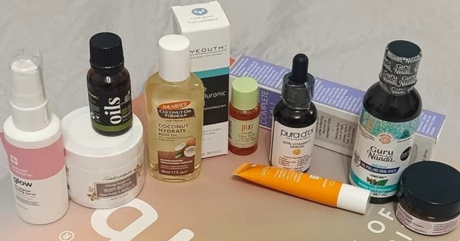An assortment of skincare and beauty products, including Palmer's body oil, a Pixi tonic, serums, and body butter arranged on a flat surface.