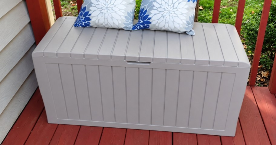 a grey plastic deck box on a back deck with pillows on top