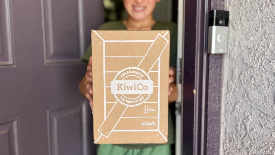 a boy at a front door of a house holding a kiwico box