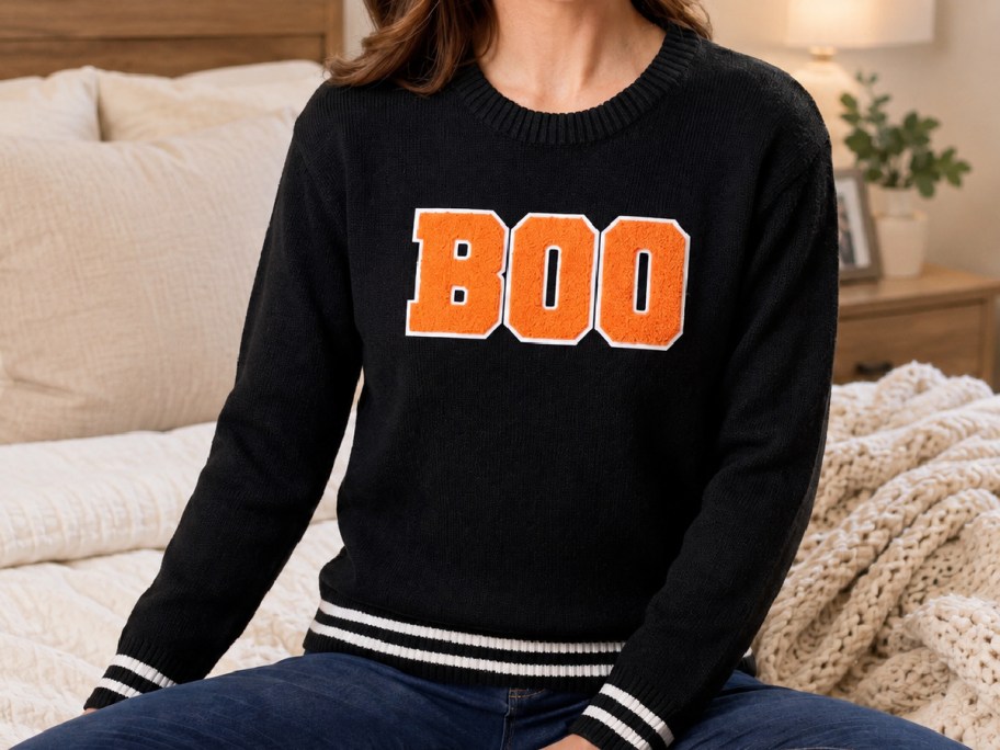 woman wearing a black halloween sweater sitting on a bed