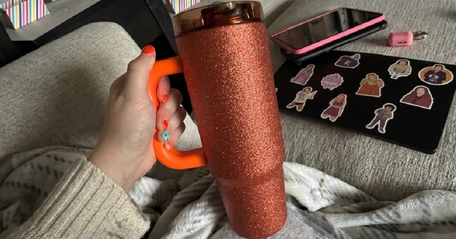 woman's hand holding an orange glitter tumbler