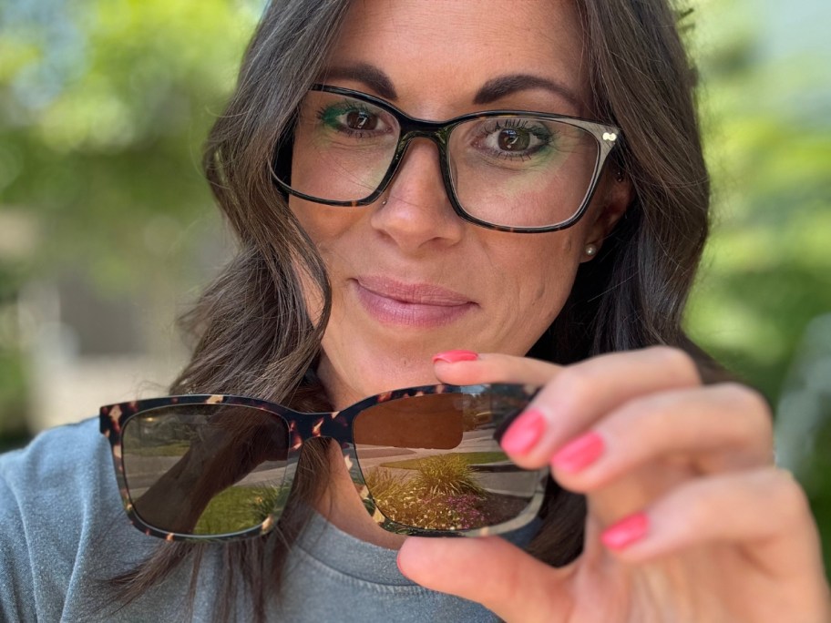 woman wearing glasses holding up a sunglasses topper
