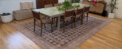A large Ruggable area rug with a vintage-style brown and beige geometric pattern placed under a dining table and chairs in a hardwood room.