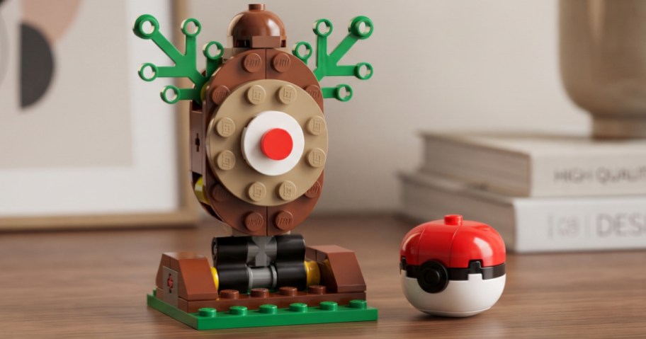 A custom Lego model of a Target bullseye logo with green branch-like antlers on a brown base, sitting next to a built Lego Poké Ball on a wooden surface.