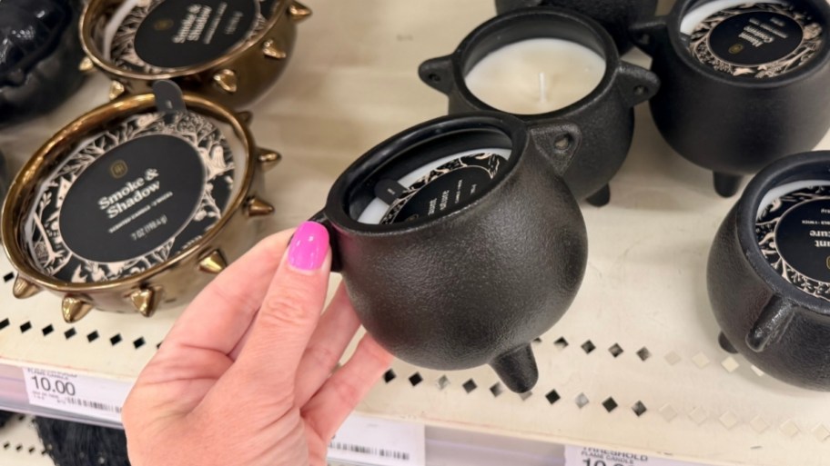 a womans hand holding a small black cauldron candle