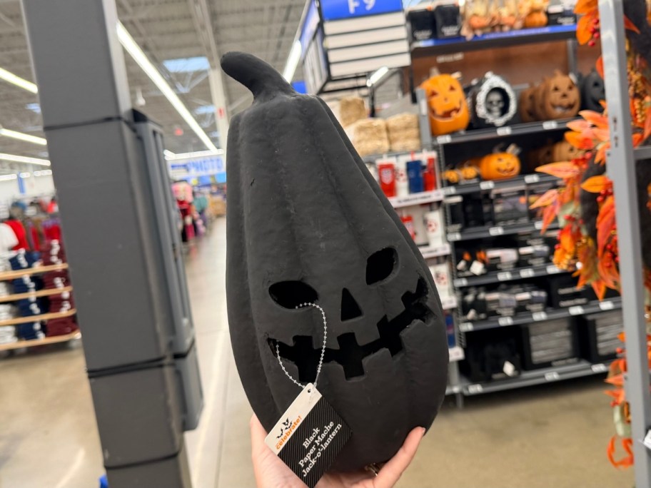 hand holding a black paper mache jack-o-lantern in a store