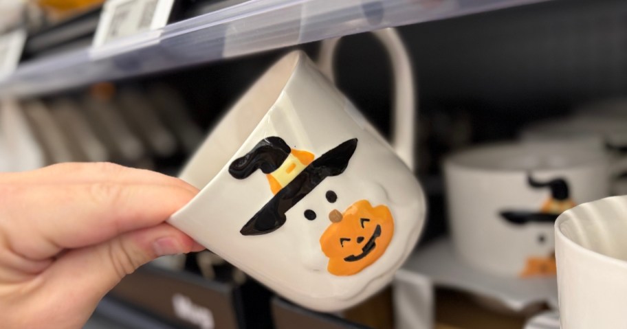 hand reaching for a Halloween mug with a ghost in a witch hat on it 