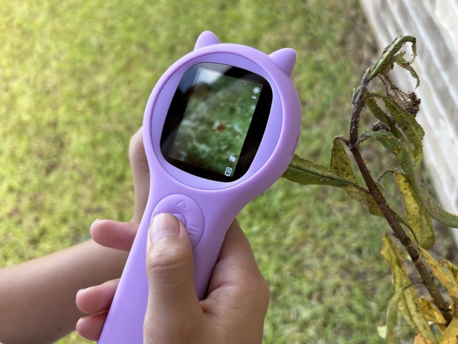 child holding a purple digital microscope near a plant