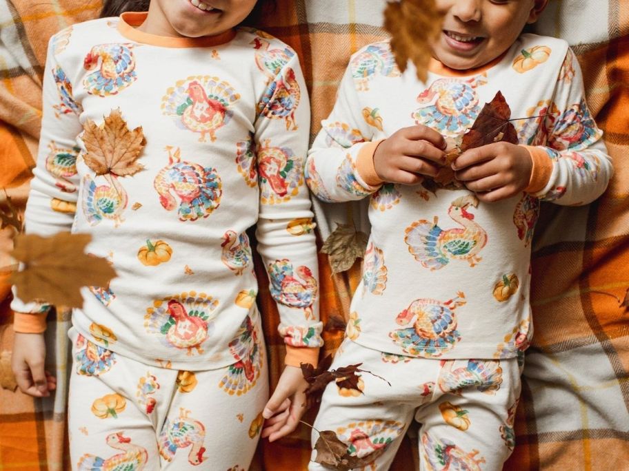 two kids laying down on a bed of leaves wearing Burt Bees two piece Thankksgiving pajamas