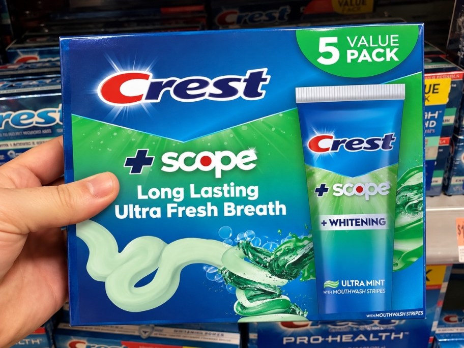 a hand holding a crest toothpaste 5 pack