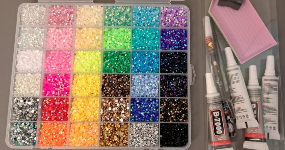 A Cusmation rhinestone bedazzling kit featuring a large organizer box filled with assorted colorful rhinestones, along with glue tubes, picking tools, and a pink tray on the side.