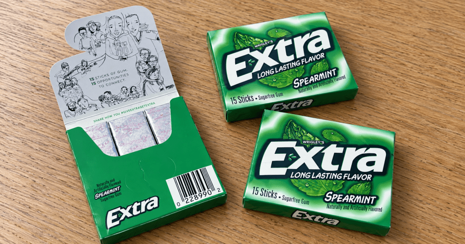 Three packs of Extra Spearmint sugar-free gum on a wooden table, with one pack open to show the wrapped sticks.