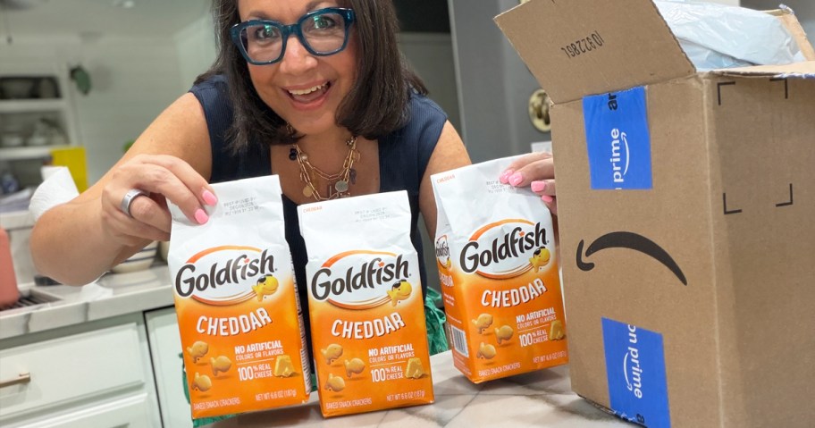 woman holding up 3 bags of goldfish next to an amazon box