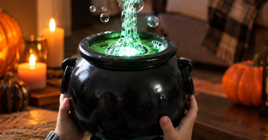hands holding a black cauldron blowing green bubbles