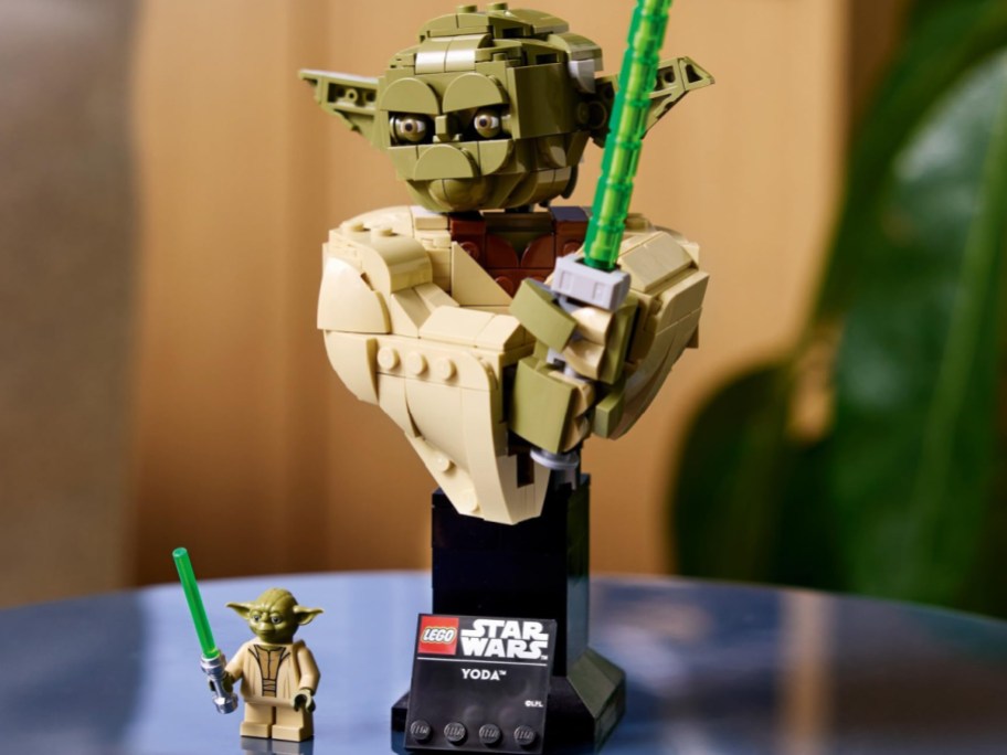 A LEGO Star Wars Yoda bust on a display stand holding a green lightsaber, accompanied by a small Yoda minifigure holding a lightsaber at the base.