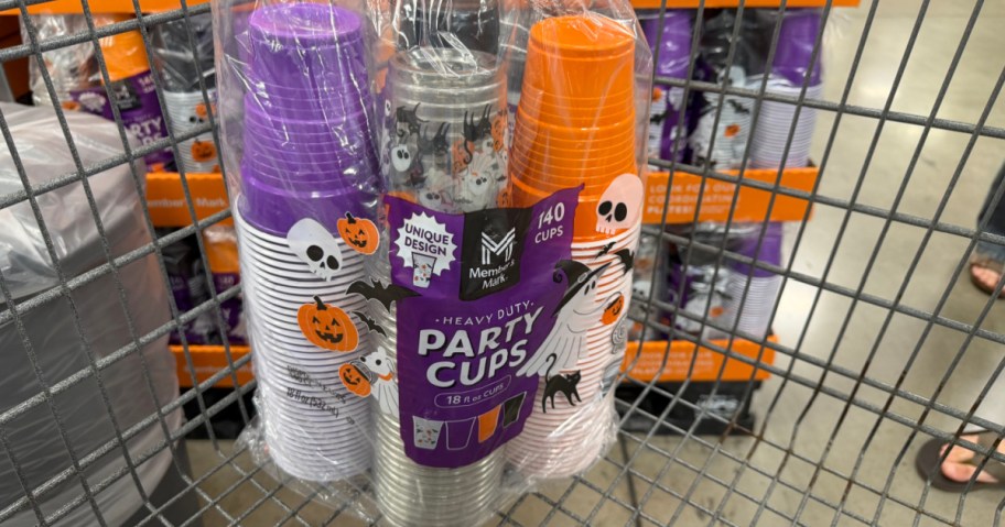 A 140-pack of Member's Mark heavy duty Halloween party cups in purple, black-and-white, and orange designs sitting inside a store shopping cart.