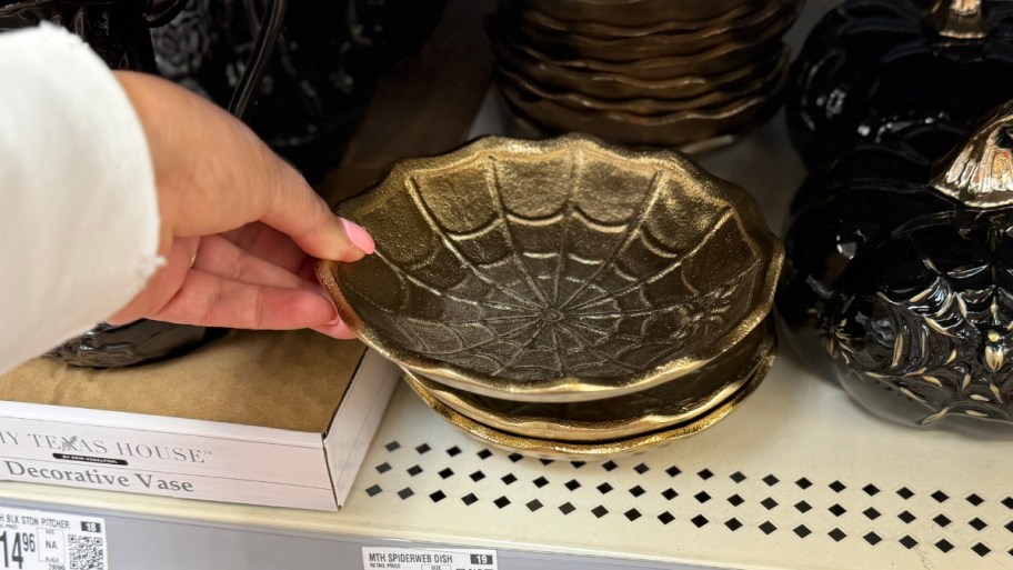 womans hand reaching for a small gold spider bowl