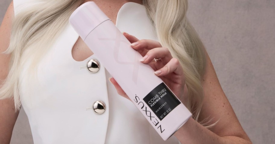 A person holding a white bottle of Nexxus Comb Thru Flexible Hold Hairspray.